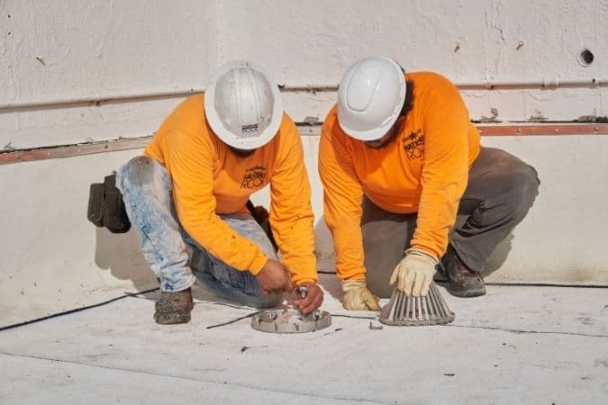 Nations Roof employees kneeling down to repair commercial roof damage