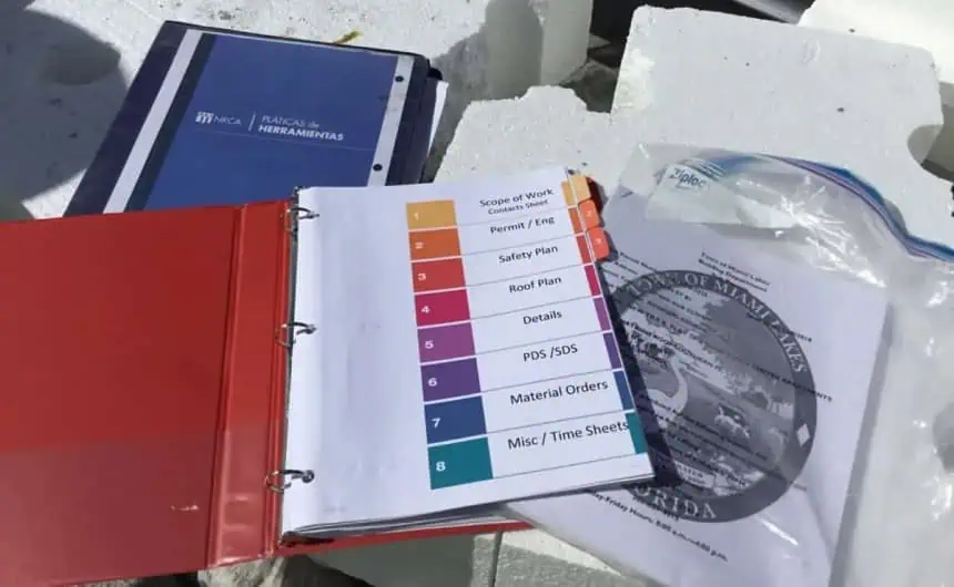 Red binder with safety and material plans at commercial roofing site, Miami.