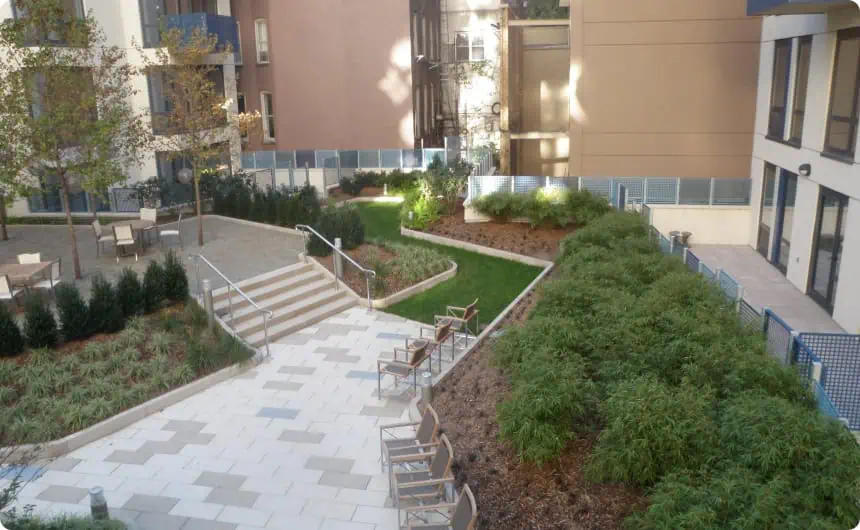 Modern courtyard with paved walkways, green plants, and metal fence at 800 10th Ave, NY