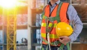 Commercial roofer with hard hat and harness at busy construction site.