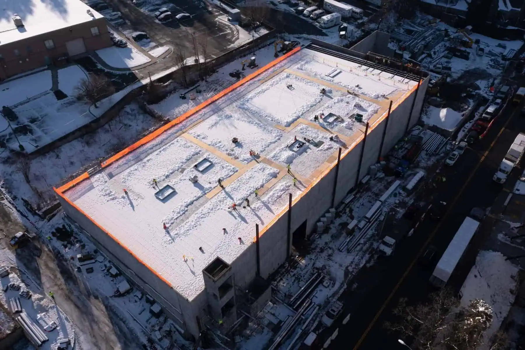 Aerial: Snowy industrial roof construction with TPO membrane and safety barriers.
