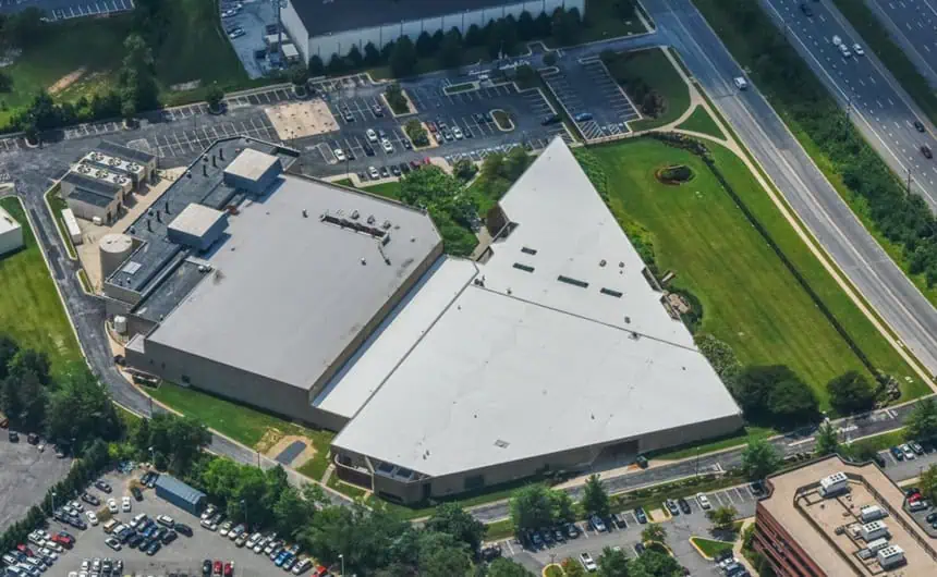 Aerial view of triangular commercial roof near highway, parking lot, and greenery