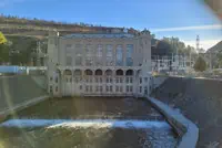 Concrete building with arched windows and industrial roofing by river.