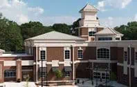 Brick building with white trim, clock tower, and glass doors; partially cloudy sky.