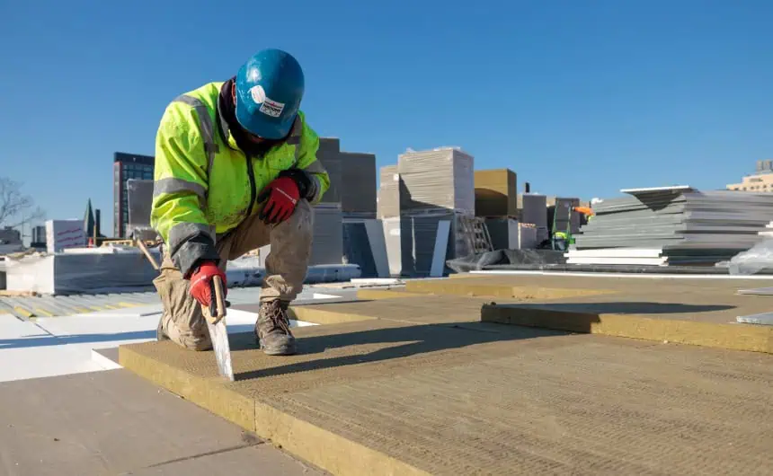 Worker trowels insulated panel on commercial roof.