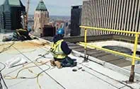 Commercial roofers installing TPO membrane with skyscraper backdrop