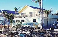 Motorhome by two-story house; debris and palm trees visible
