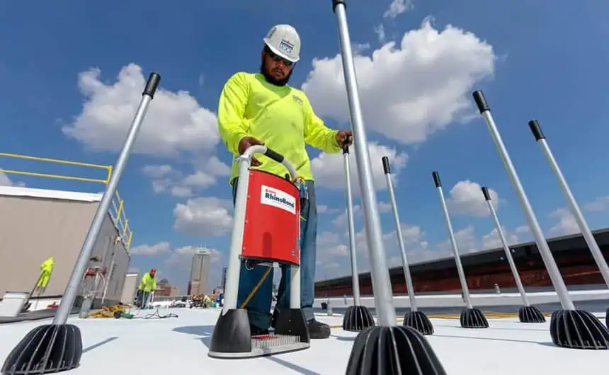 Construction worker installing rooftop equipment on industrial building, surrounded by safety poles.