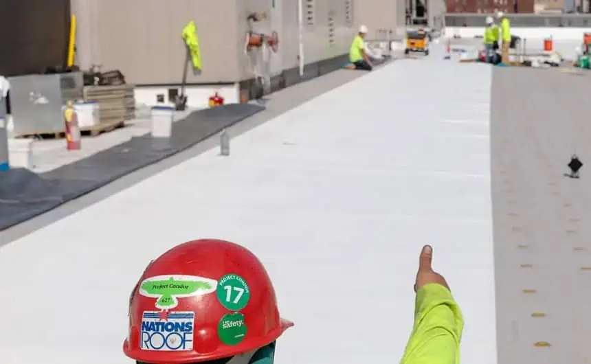 Construction worker in red hard hat on commercial roof installation with crew and equipment.