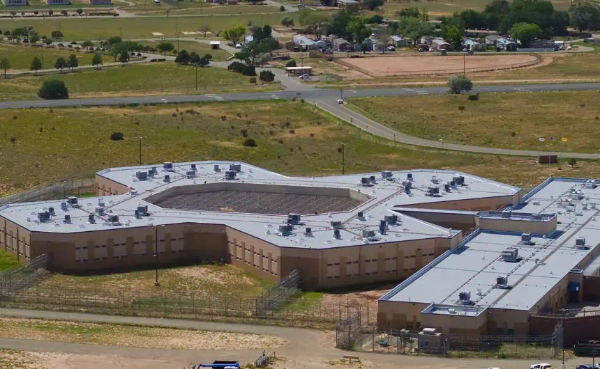 Aerial view: Complex star-shaped correctional facility with commercial roofing, Santa Fe County.