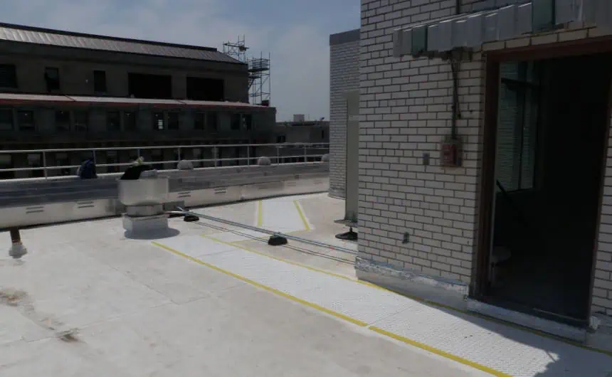 White-tiled rooftop with safety markings, cables, and urban background. Commercial flat roof inspection.