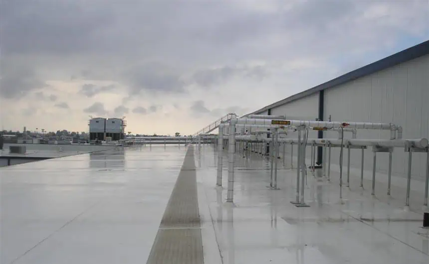 White-coated flat commercial roof with safety-marked pipes under overcast sky