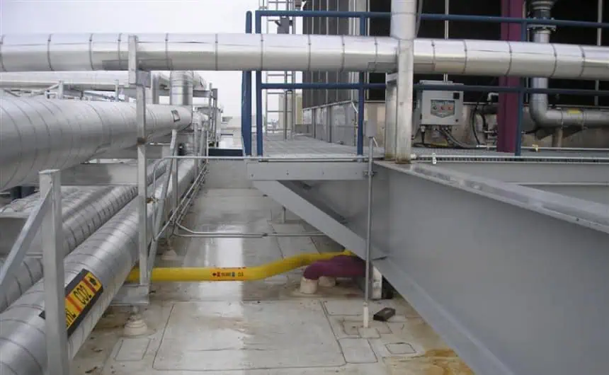 Industrial rooftop with pipelines, walkways, machinery, and safety barriers.