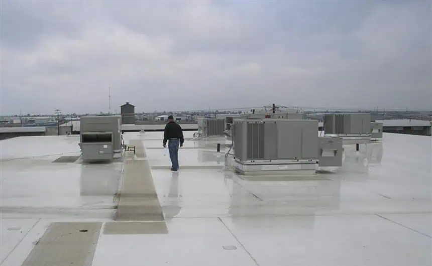 Technician navigating HVAC units on commercial flat rooftop under cloudy sky.