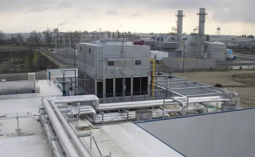 Industrial facility with cooling towers, pipes, under cloudy sky on robustly engineered rooftop.