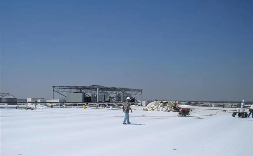 Commercial flat roof installation: worker amid equipment under clear blue sky.
