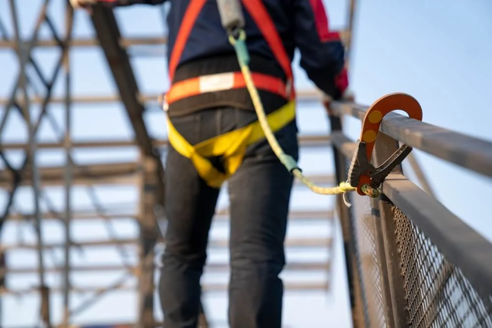 A worker in a safety harness inspects a metal structure on a flat roof, emphasizing commercial roofing safety and EPDM maintenance.