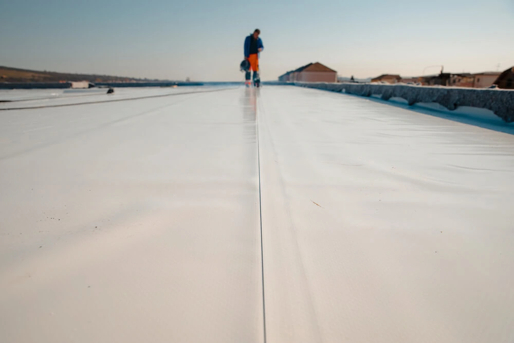 A worker in the distance welding seams between sheets of TPO roofing membrane.